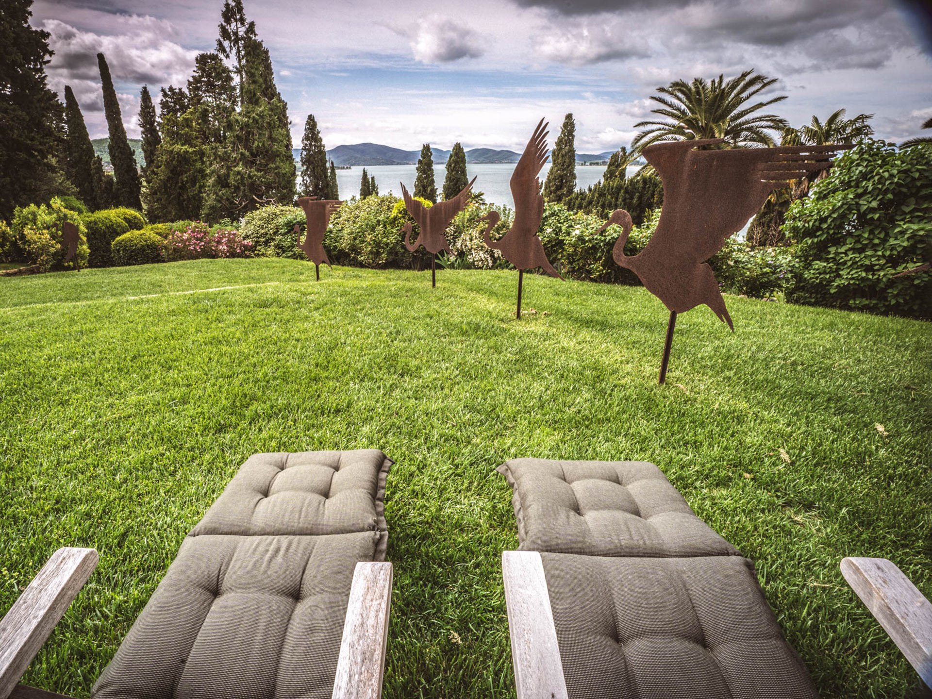 Due lettini su un prato circondato da siepi, oltre le quali si può ammirare la veduta del lago.